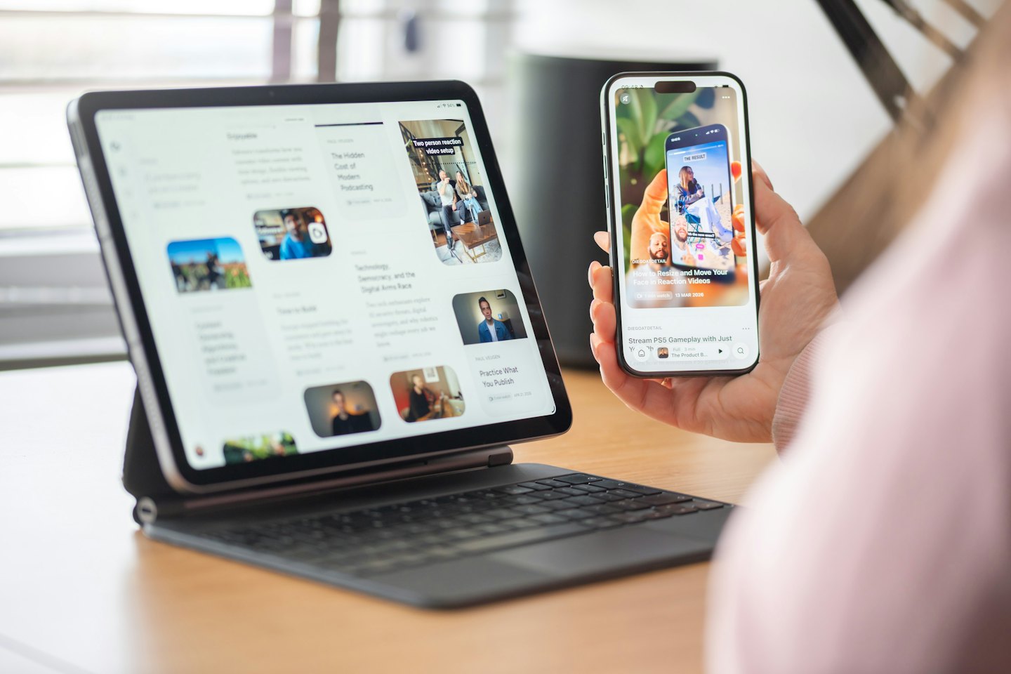 Ruce držící smartphone a tablet na dřevěném stole.